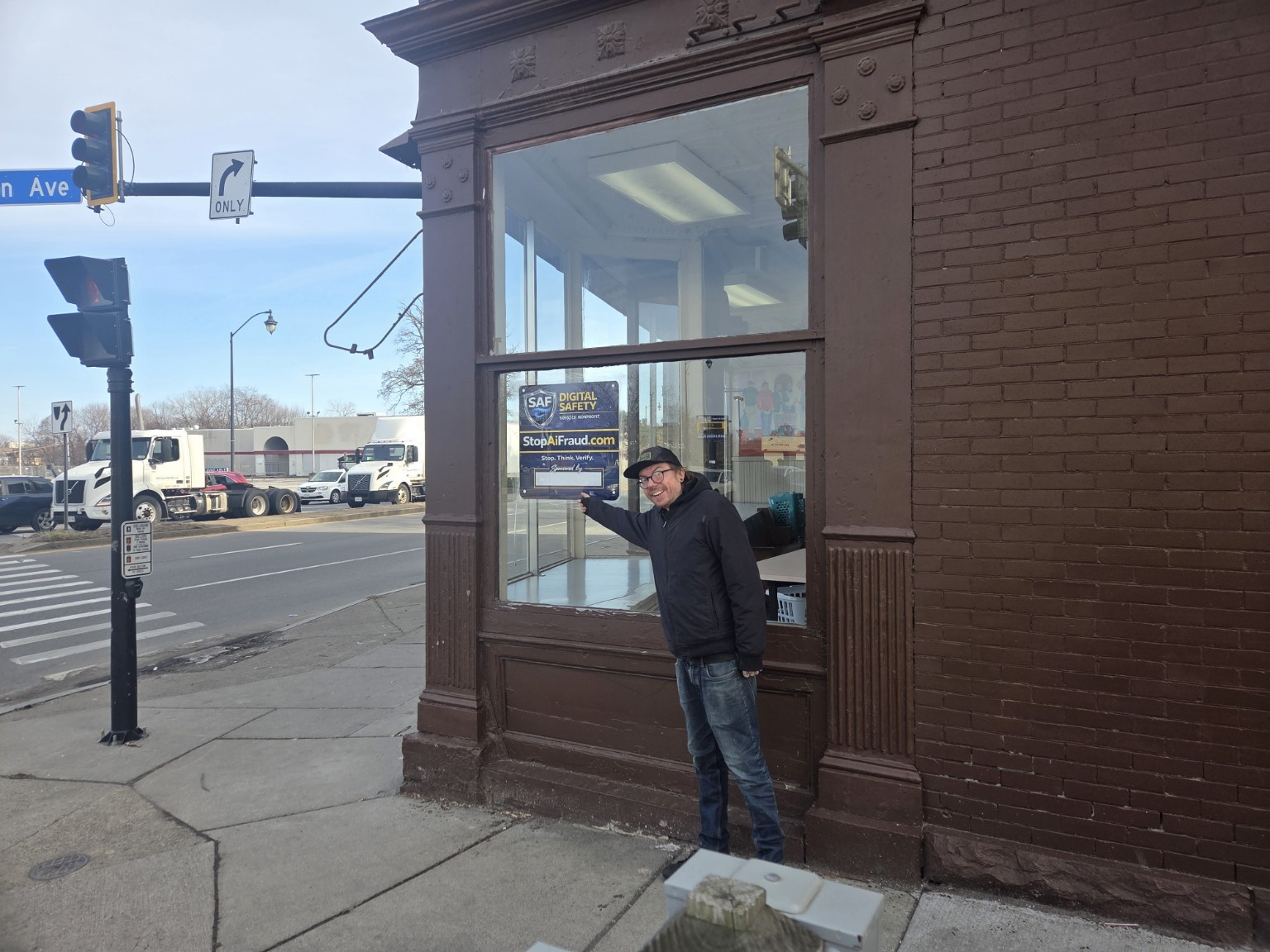 SAF founder pointing to the StopAiFraud Digital Safety Community Support sign in the window of the Rochester outreach storefront.